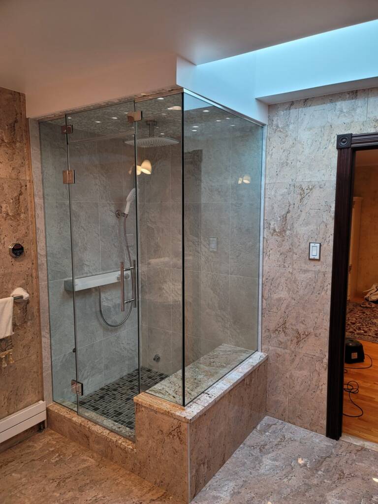 Frameless glass shower enclosure with stone tile in a New York City bathroom