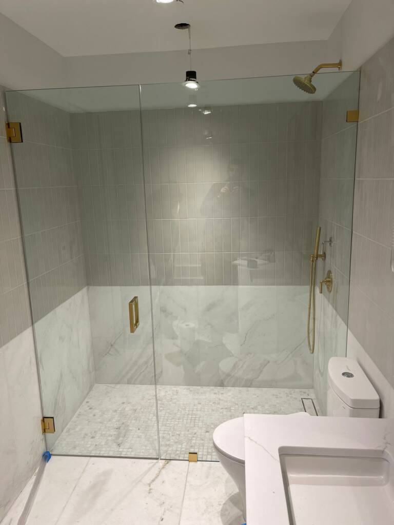 Large frameless glass shower panel in a marble NYC bathroom